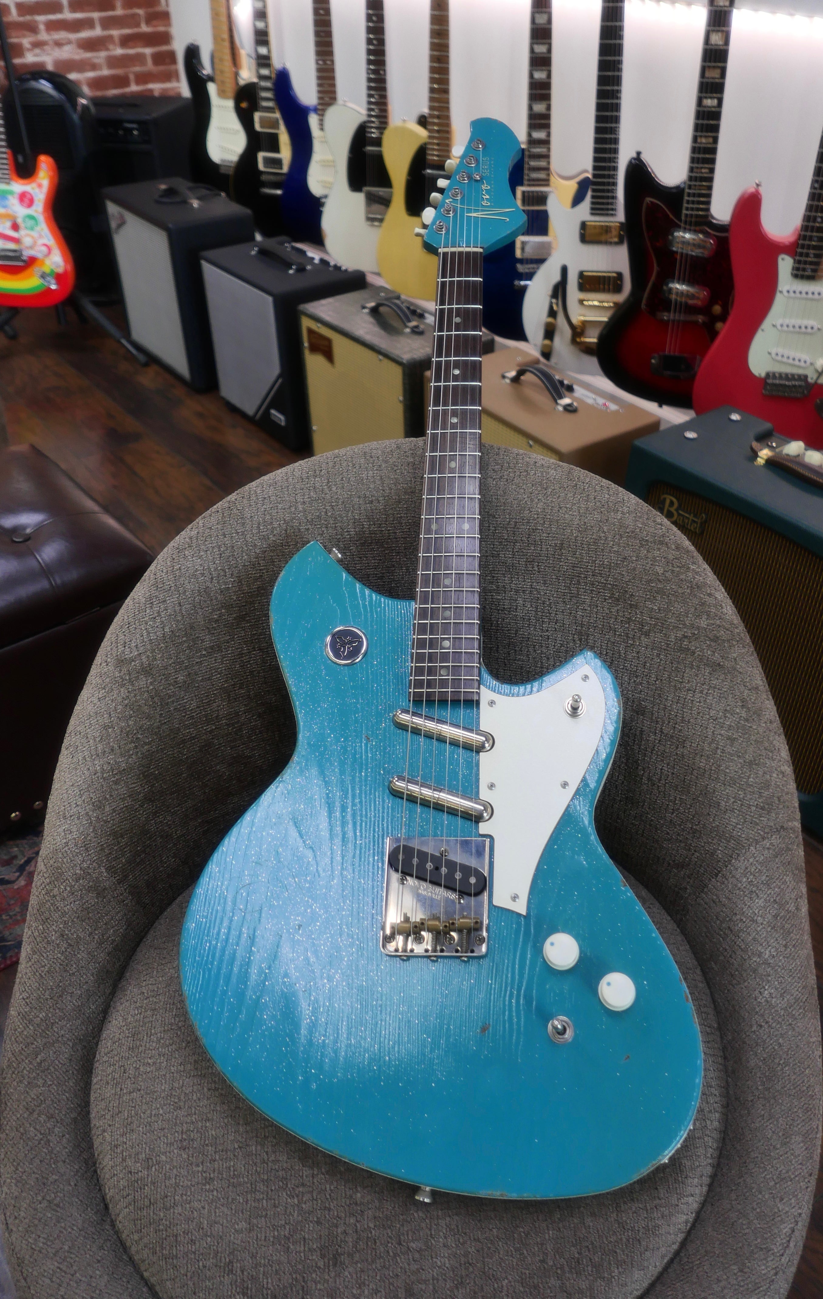 Novo Serus T Taos Turquoise guitar displayed on a chair with other guitars in the background.